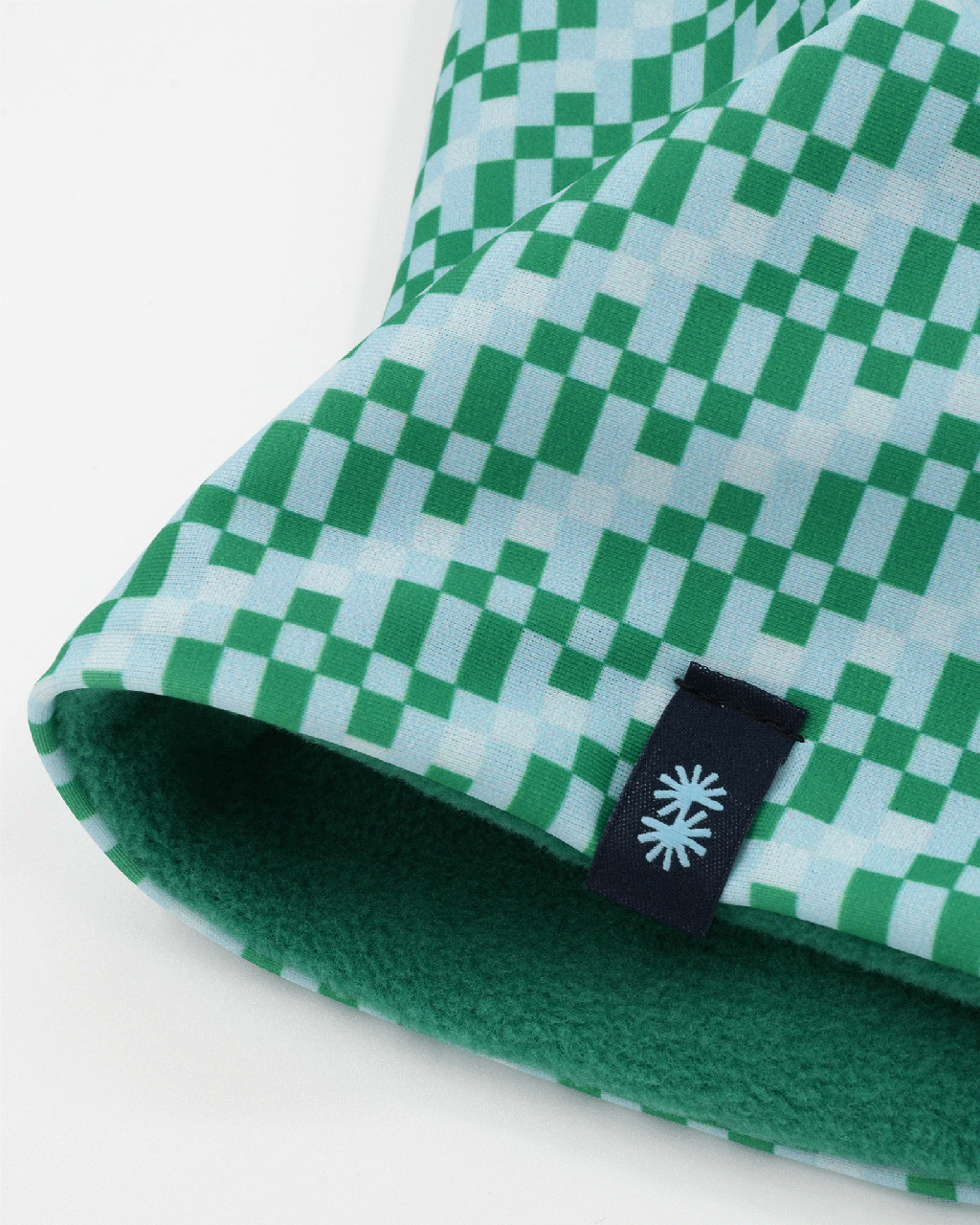 Close-up view of a double layer neck warmer with a green, gray and white checkered printed lycra, green fleece lining and black CTW logo woven label