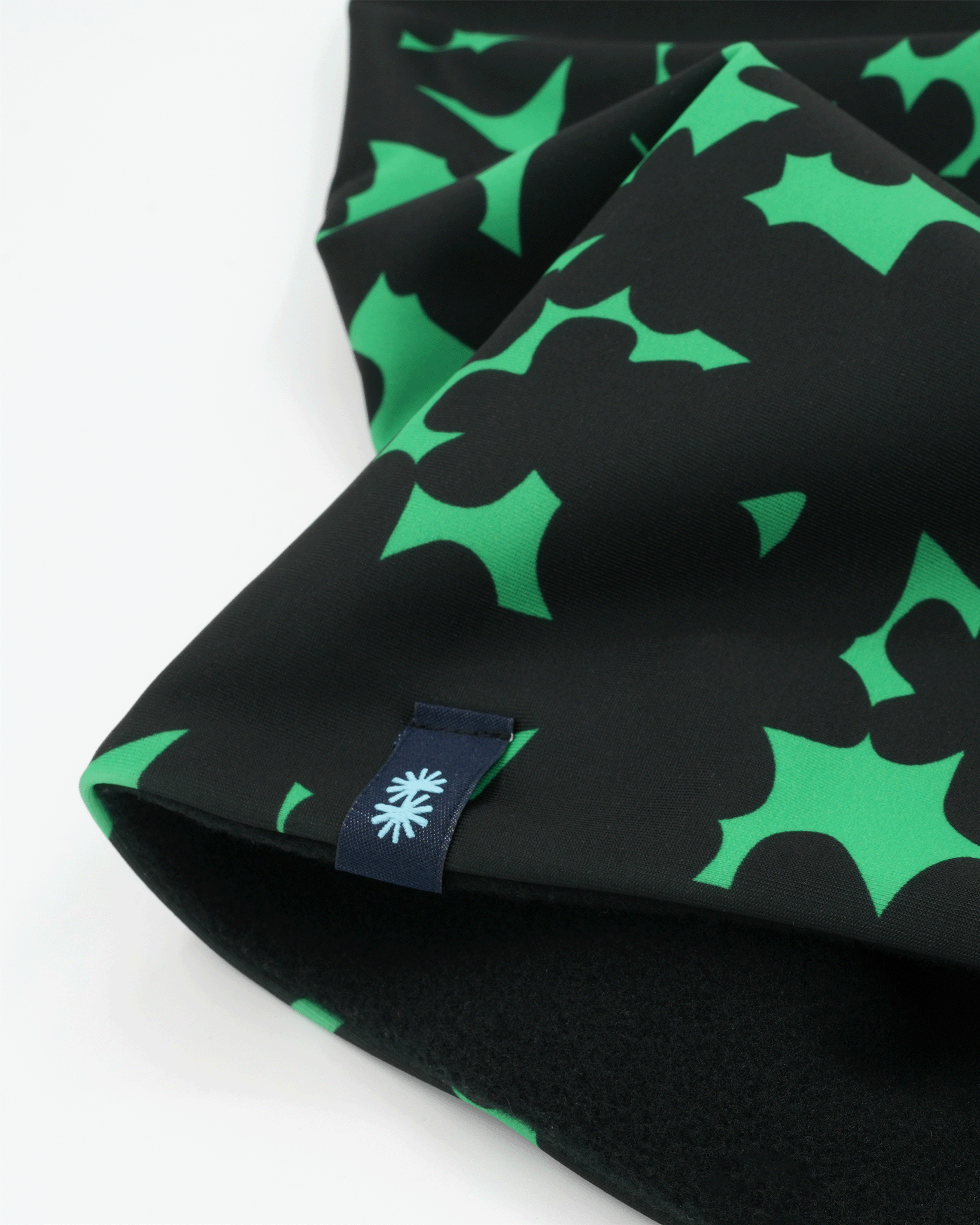 Close-up of a double layer neck warmer with black and green floral printed lycra,  black fleece lining and black CTW logo woven label