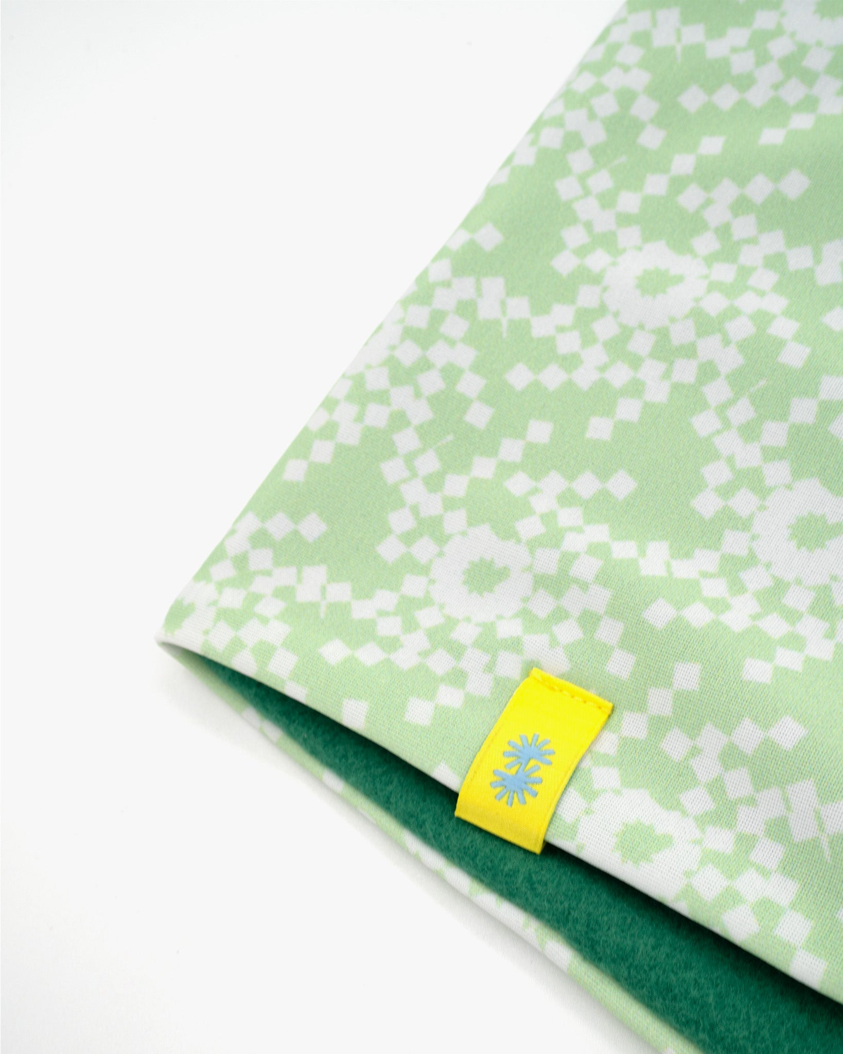 Close-up of a double layer neck warmer with green and white geometric snowflake printed lycra, green fleece lining and yellow woven CTW logo label