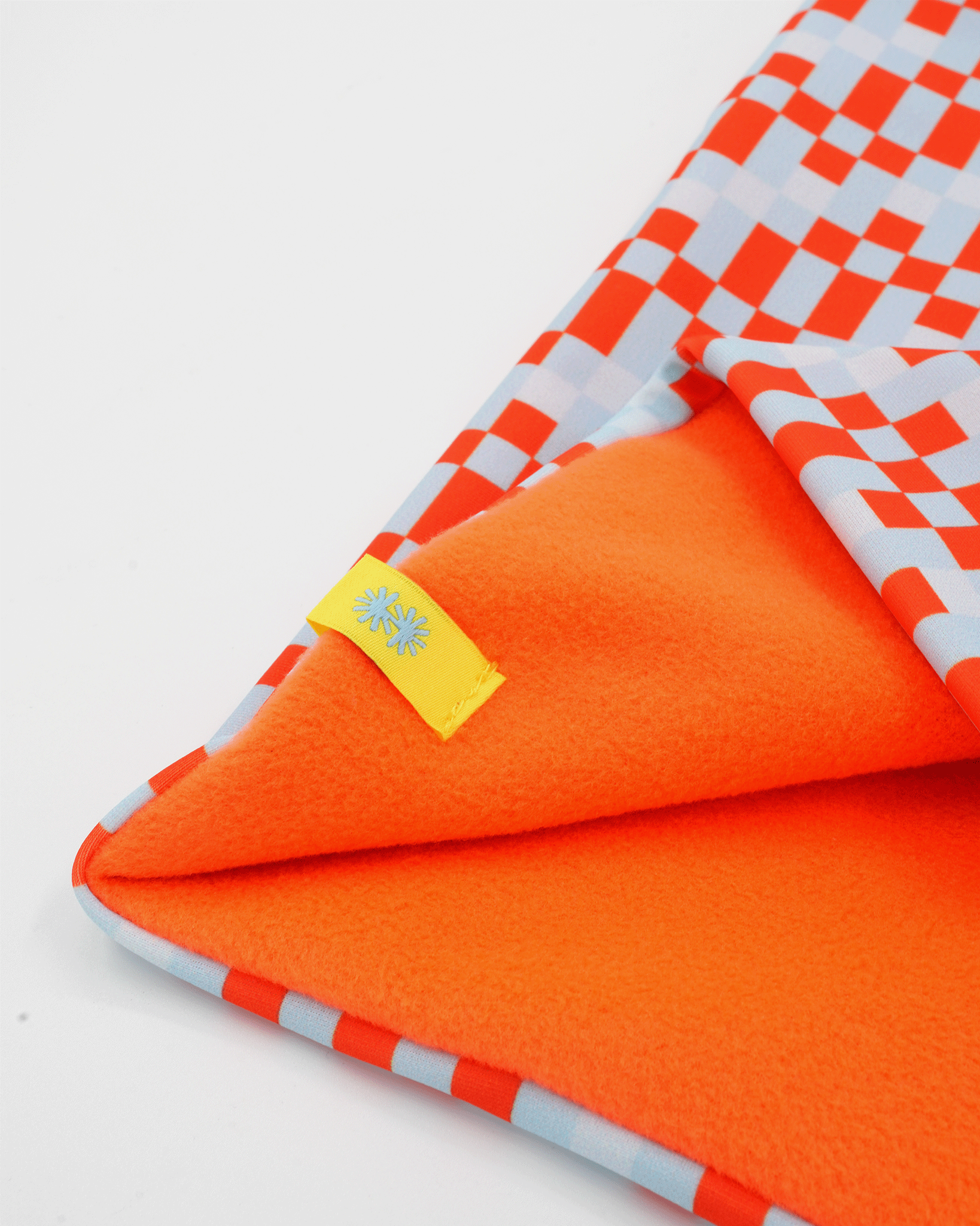 Close-up view of a double layer neck warmer with a red, gray and white checkered printed lycra, orange fleece lining and yellow CTW logo woven label