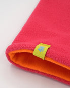 Close-up view of a polartec fleece pink front and orange back reversible neck warmer, with a yellow CTW logo woven label