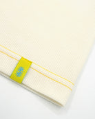 Close-up view of a long off-white Power Wool neck gaiter, with a yellow back seam and yellow CTW logo woven label