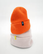 Orange cashmere merino wool beanie stacked on top of off-white cashmere merino wool beanie