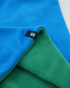 Close-up view of a polartec fleece blue front and green back reversible neck warmer, with a black CTW logo woven label